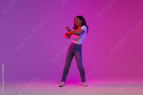 Cheerful Young Black Female Dancing in Neon Light Over Purple Background