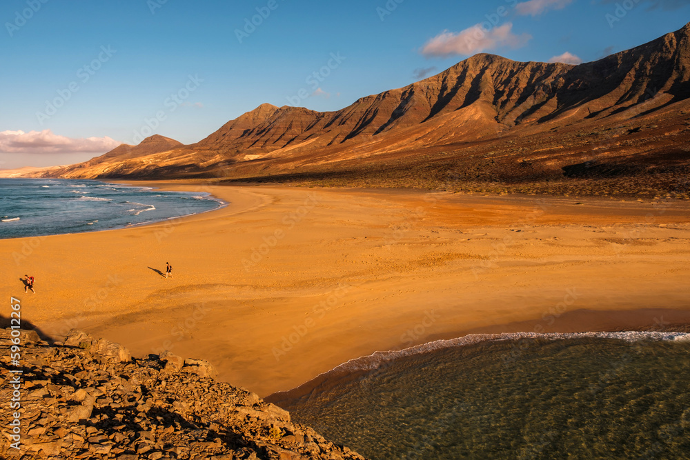 Cofete Beach with unknown tourists at sunset on the Canary Island Fuerteventura, view from the little La Islotta.
