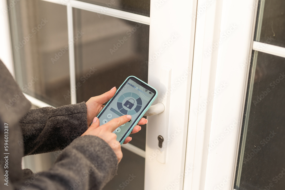 Woman setting alarm in her apartment via smartphone application when leaving home Woman setting alarm in her apartment via smartphone application when leaving home