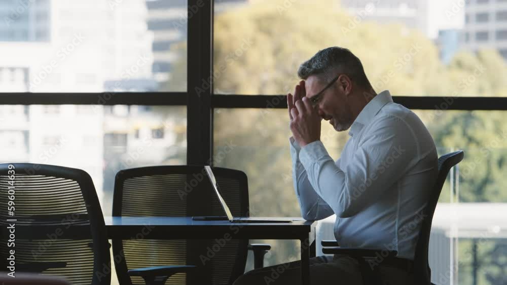 Side view of stressed or tired mature businessman working on laptop sitting at boardroom table - shot in slow motion Side view of stressed or tired mature businessman working on laptop sitting at boardroom table - shot in slow motion