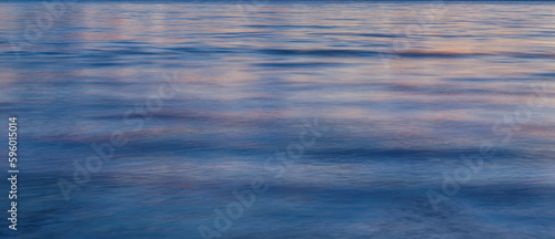 Fotografie Sea surface background. Blue and pink water at sunset texture.