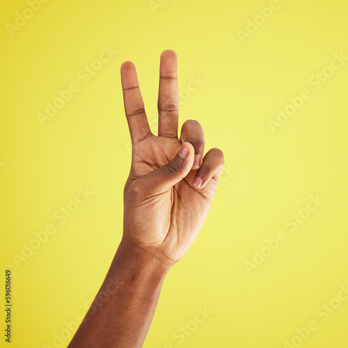 I like it twice. Studio shot of an unrecognisable man making a peace sign against a yellow background.