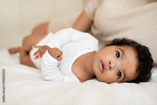 Cute african american small child in white clothes lie, sleep on soft bed in bedroom interior, close up