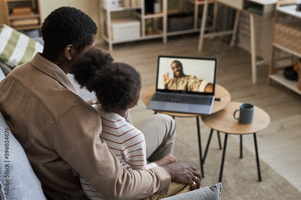 Rear view of dad sitting on sofa with his daughter, they having video call on laptop with their military mom Rear view of dad sitting on sofa with his daughter, they having video call on laptop with their military mom