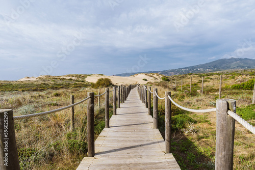 Empty  wooden boardwalk on a beach Praia do Guincho in Sintra. View of grass and sand with hills and Atlantic Ocean in the background