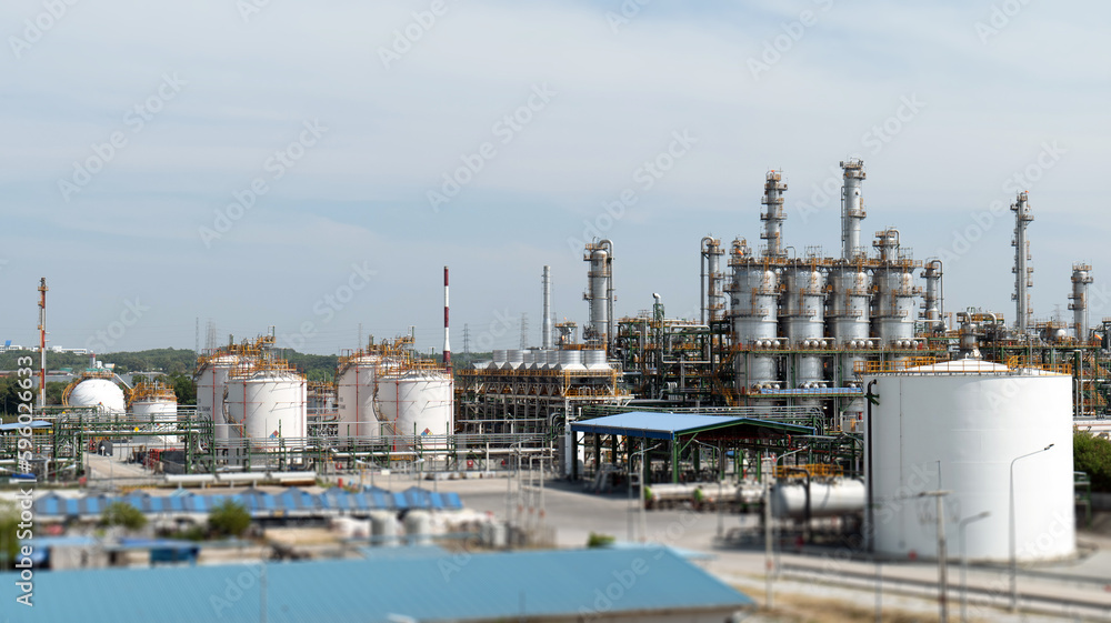A chemical or petrochemical facility, an oil refinery plant with steel pipes and chimney cooling towers, and a landscape with a blue sky in the background. A chemical or petrochemical facility, an oil refinery plant with steel pipes and chimney cooling towers, and a landscape with a blue sky in the background.