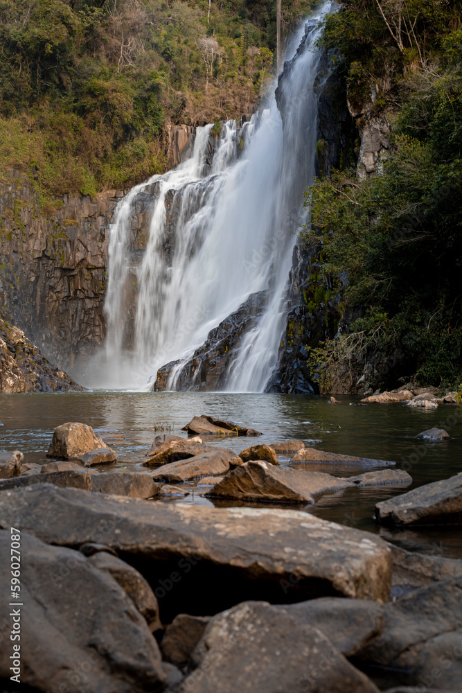 Obraz premium Cachoeira com rochas atrás em tons de marrom e água caindo em um lago