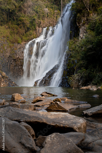 Cachoeira com rochas atrás em tons de marrom e água caindo em um lago