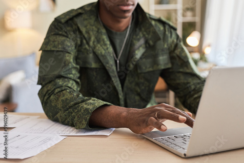 Close-up of military young man sitting at table at home and typing on laptop, he doing online work