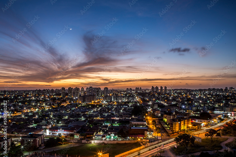 Sunset seen from above the building with orange and blue colored sky with the moon in the center and avenues and buildings highlighted. | Avenida Ayrton Senna em Natal, RN. Sunset seen from above the building with orange and blue colored sky with the moon in the center and avenues and buildings highlighted. | Avenida Ayrton Senna em Natal, RN.