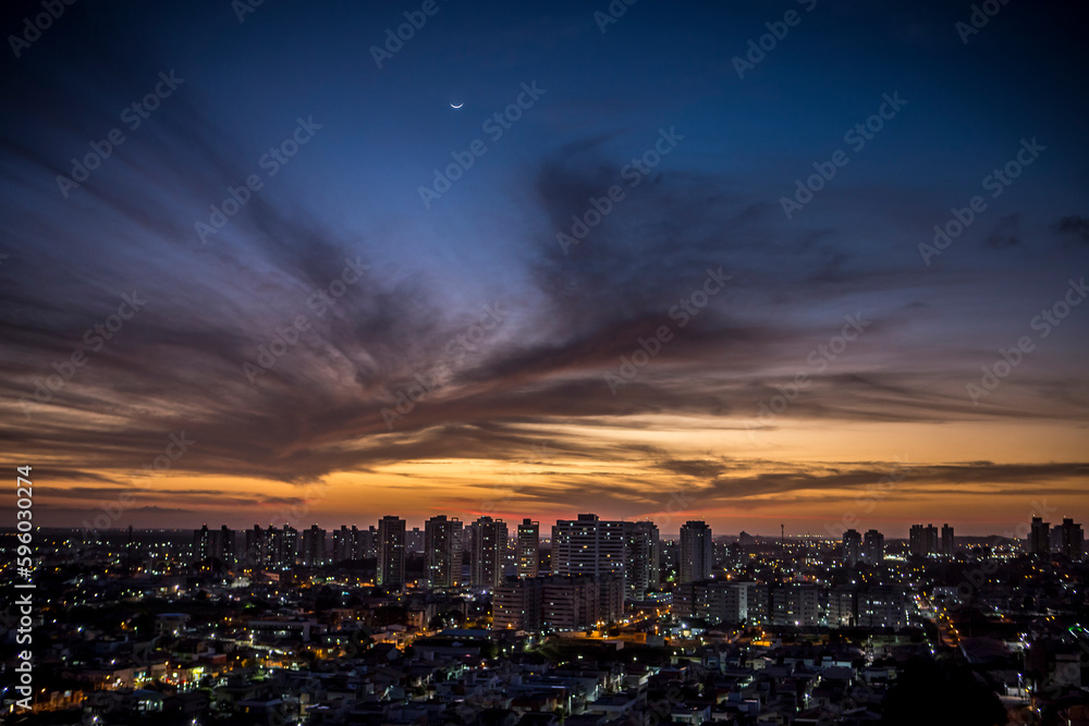 Sunset seen from above the building with orange and blue colored sky with the moon in the center and avenues and buildings highlighted. | Avenida Ayrton Senna em Natal, RN.