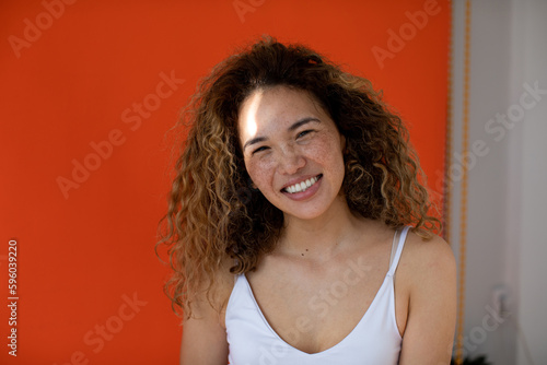 Smiling woman with curly hair and freckles on her face on orange background.