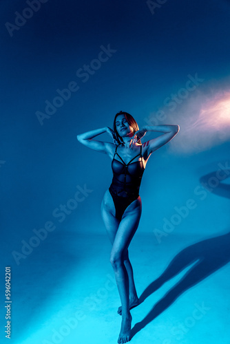 Sexy woman in black bodysuit posing in studio in colored neon light © Darius
