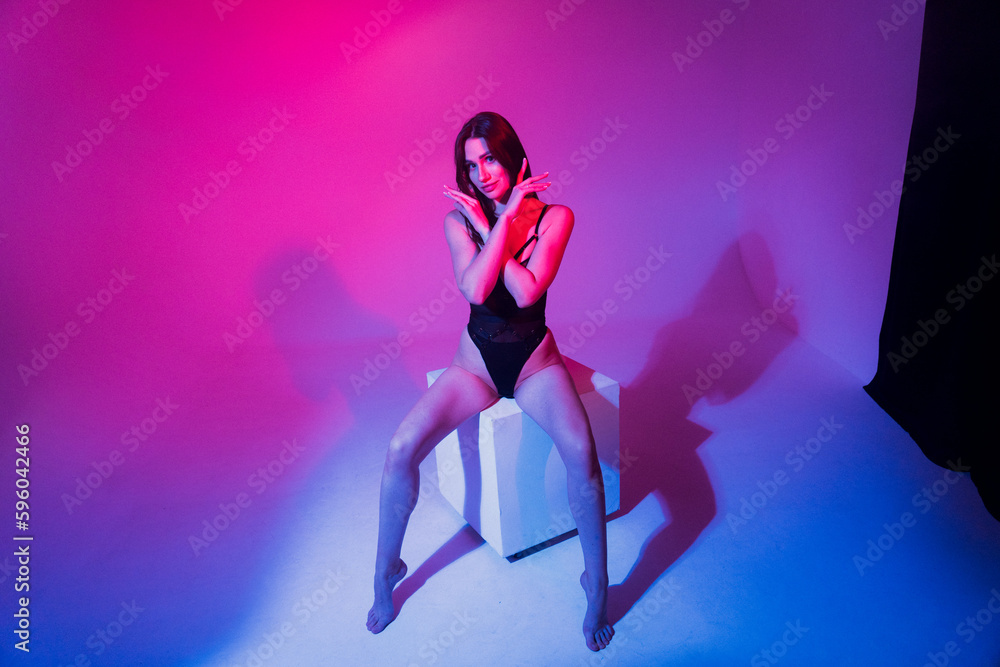 Sexy woman in black bodysuit posing in studio in colored neon light