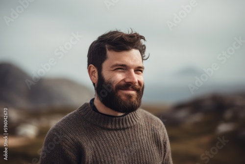 Portrait of a handsome young man with a beard and mustache in a knitted sweater against the background of a mountain landscape