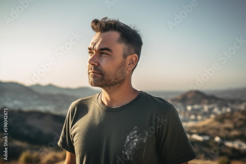 Handsome young man standing on top of a mountain and looking away