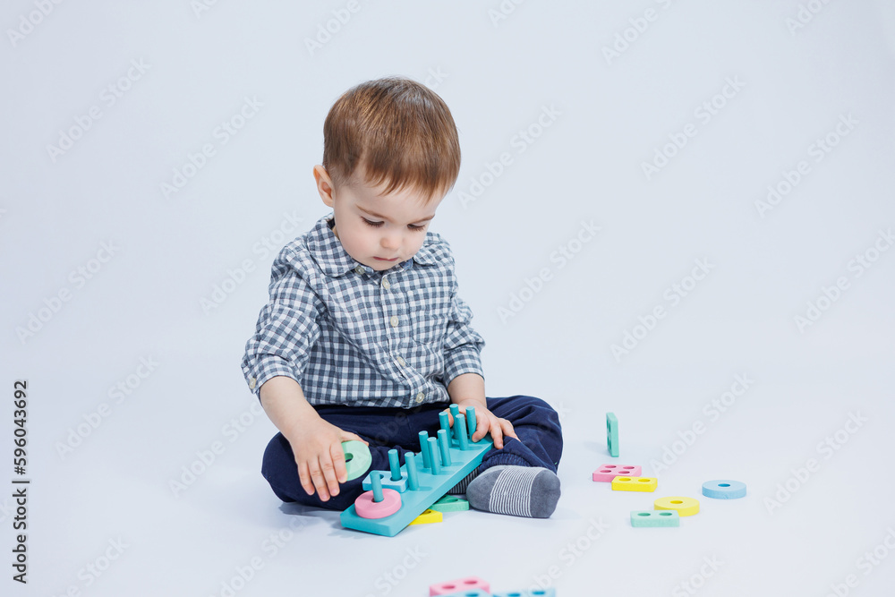 A cute little boy in a checkered shirt sits on a white background and plays with wooden educational toys. Ecological wooden toys for children A cute little boy in a checkered shirt sits on a white background and plays with wooden educational toys. Ecological wooden toys for children