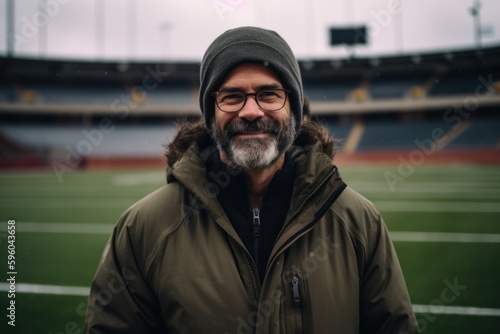 Portrait of a smiling bearded man in a warm jacket and glasses on the background of a football stadium © Robert MEYNER