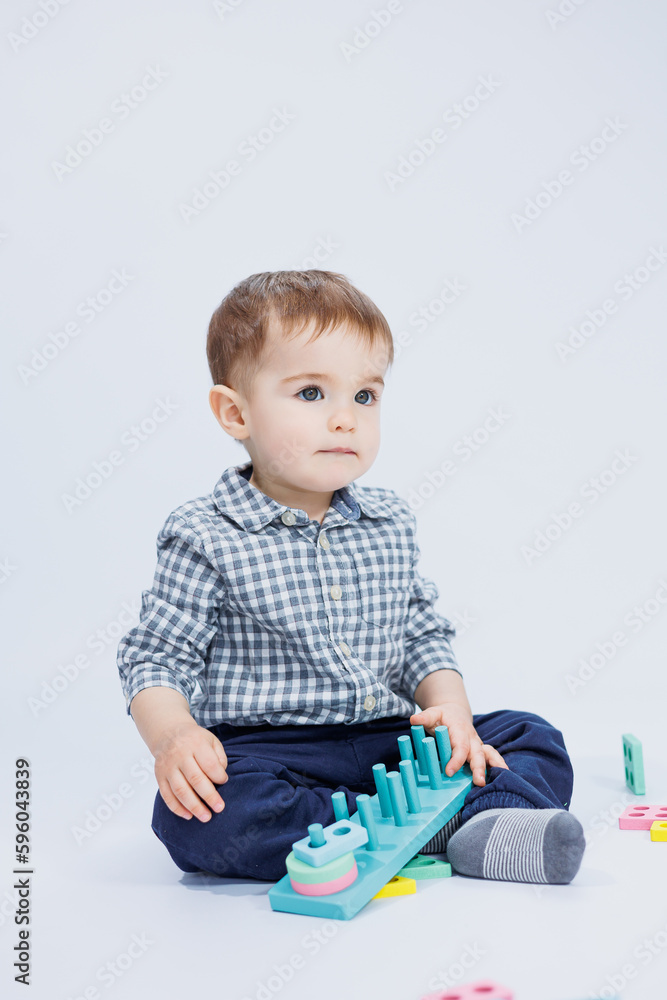 A cute little boy in a checkered shirt sits on a white background and plays with wooden educational toys. Ecological wooden toys for children A cute little boy in a checkered shirt sits on a white background and plays with wooden educational toys. Ecological wooden toys for children