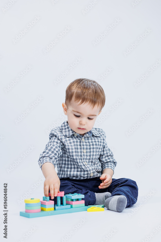 A little boy in a shirt is building a colorful wooden toy on a white background. The concept of children's development, games for children, toys. Copy space