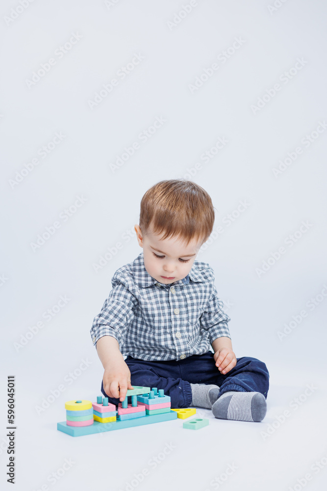 A little boy in a shirt is building a colorful wooden toy on a white background. The concept of children's development, games for children, toys. Copy space A little boy in a shirt is building a colorful wooden toy on a white background. The concept of children's development, games for children, toys. Copy space