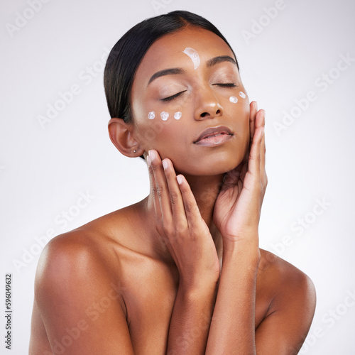 Dotted to perfection. Studio shot of an attractive young woman applying lotion to her face against a grey background.