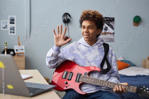 Photo Happy teenager in casualwear greeting his music teacher by waving hand while sit