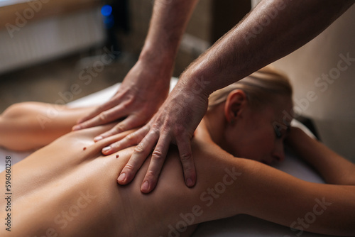 Close-up cropped shot of hands unrecognizable masseur massaging back and shoulder blades of young woman lying on massage table. Concept of body care and rehabilitation of spiritual peace.