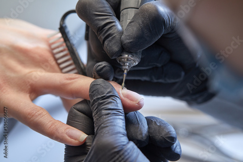 Manicure process in beauty salon  cleaning of nails by a milling cutter. Manicurist filing client s nails at table. Removing the nail plate with a milling machine. nail care concept