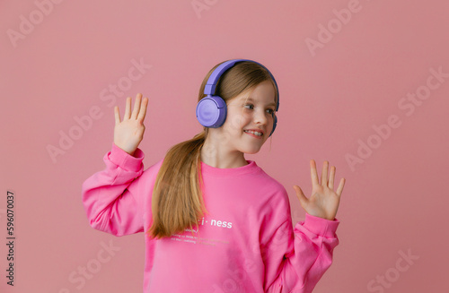 Photo of a cute funny young teenage girl in a pink jumper  headphones  dancing  enjoying music on a background
