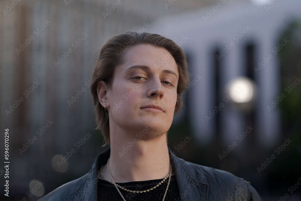 Expressing tranquility, happiness, and their queer, fluid gender identity, a genderfluid model poses with a calm, direct gaze while standing on the sidewalk in the later afternoon sun. Expressing tranquility, happiness, and their queer, fluid gender identity, a genderfluid model poses with a calm, direct gaze while standing on the sidewalk in the later afternoon sun.