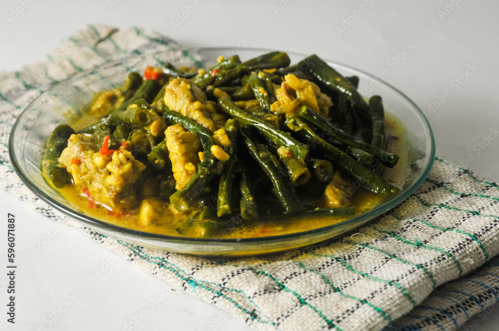 long bean vegetables and sliced tempeh with coconut milk sauce served on a small plate and a napkin isolated on a white background long bean vegetables and sliced tempeh with coconut milk sauce served on a small plate and a napkin isolated on a white background