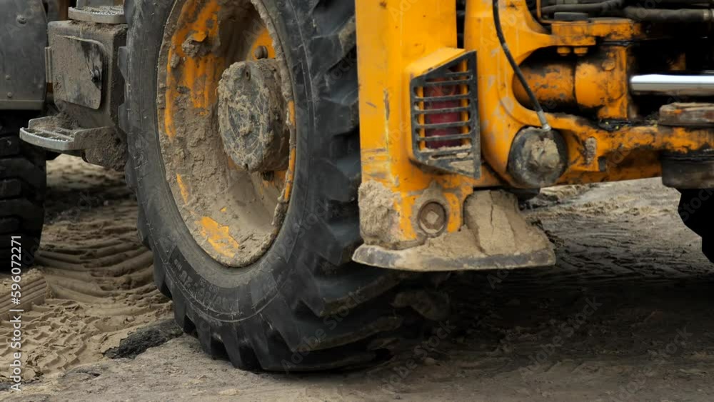 Tractor excavator rides in reverse during repair work at a construction site. Repair of communications in the city. The loader backs up. Close-up of the big wheels of a driving tractor. Tractor excavator rides in reverse during repair work at a construction site. Repair of communications in the city. The loader backs up. Close-up of the big wheels of a driving tractor.