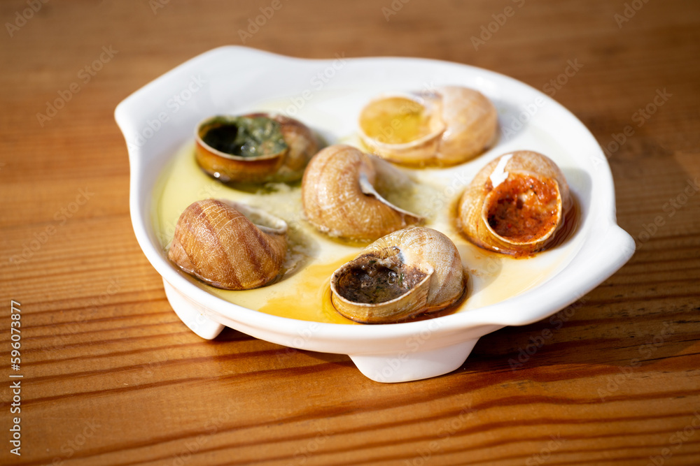 Cooked escargot snails with various sauces on a white dish on a wooden table. Cooked escargot snails with various sauces on a white dish on a wooden table.