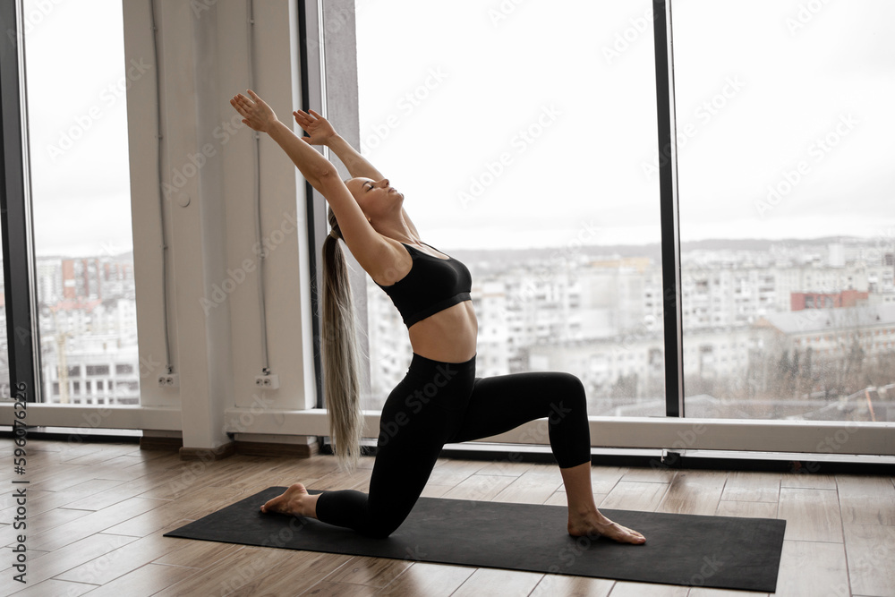 Athletic adult female in yoga clothes achieving High Lunge Pose in spacious meditation room with panoramic view. Relaxed young practitioner breathing during Utthita Ashwa Sanchalanasana exercise. Athletic adult female in yoga clothes achieving High Lunge Pose in spacious meditation room with panoramic view. Relaxed young practitioner breathing during Utthita Ashwa Sanchalanasana exercise.