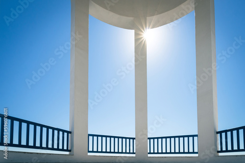 View to blue sky with the sun in shape of a star through columns of a rotunda.
