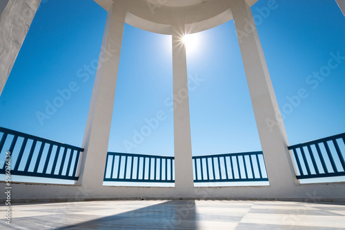 View to blue sky with the sun in shape of a star through columns of a rotunda.