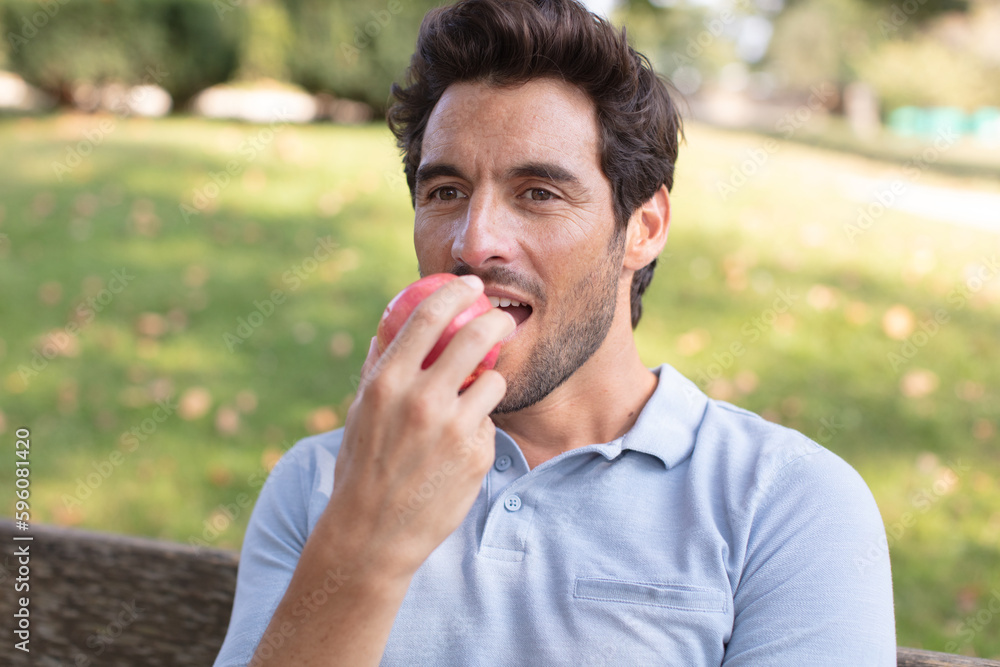 young man is eating apple in park after work young man is eating apple in park after work