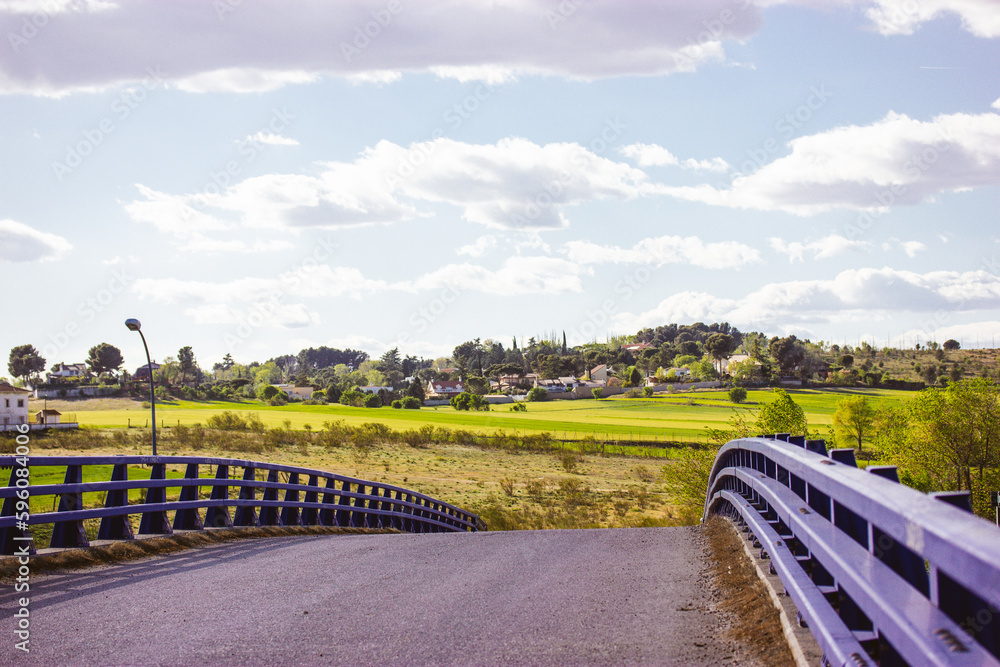 Overpass bridge against blue sky. Asphalt paved road, metal guardrails at midday in warm summer sunny day. Straight pathway goes down over a horizon. Rural street scene. Infrastructure in a village