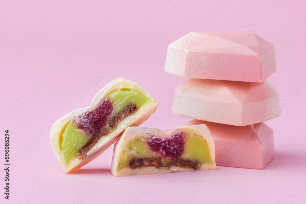 Set of homemade pink heart-shaped chocolate bonbons. Assortment of hand painted candies. Candy cut in a half. Mockup with a copy space. Macro shot of  chocolatier products on pink background