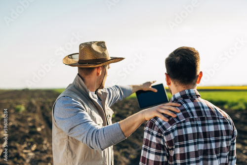 View from behind of two farmers examining crops on the field