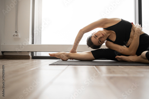 Close up of beautiful young woman doing stretching yoga side bend at airy fitness center. Panoramic windows on background. Concept of healthy lifestyles and wellness.