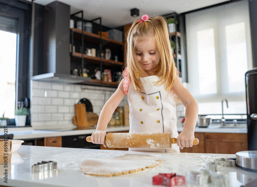 Cute little girl rolling the dough with a rolling pin to make sugar cookies Cute little girl rolling the dough with a rolling pin to make sugar cookies