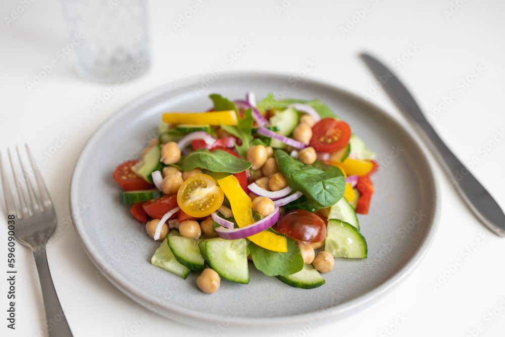 Close-up of a salad of chickpeas and fresh vegetables and lettuce leaves on a white table. Vegetarian food rich in proteins. Ideal for vegans for lunch or dinner. Close-up of a salad of chickpeas and fresh vegetables and lettuce leaves on a white table. Vegetarian food rich in proteins. Ideal for vegans for lunch or dinner.