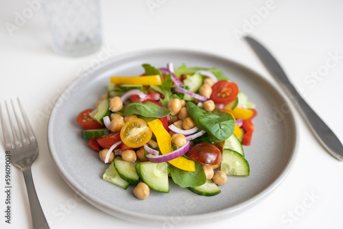 Close-up of a salad of chickpeas and fresh vegetables and lettuce leaves on a white table. Vegetarian food rich in proteins. Ideal for vegans for lunch or dinner.