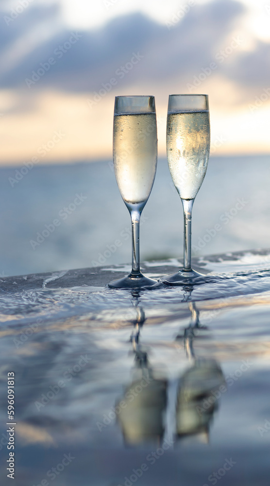 Two glasses of champagne on the side of the infinity pool against the backdrop of a sunset in the Maldives Two glasses of champagne on the side of the infinity pool against the backdrop of a sunset in the Maldives