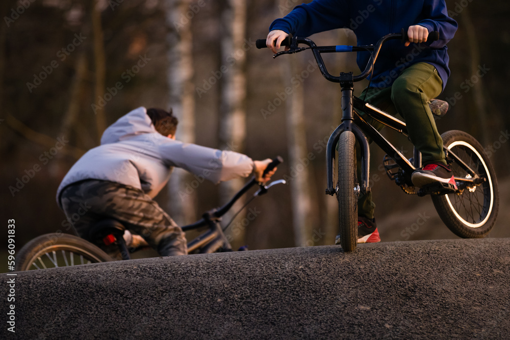 Fototapeta premium Closeup Kid boy with bicycle on a pump track park in sunset light. Asphalted bicycle race track, kids playground