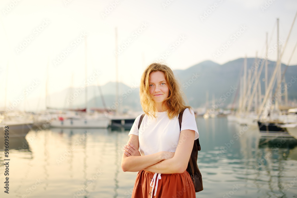 Charming young tourist woman travel by Mediterranean coast. Attractive red-haired girl on the background of sea and yachts. Yacht rental. Tourism and travel