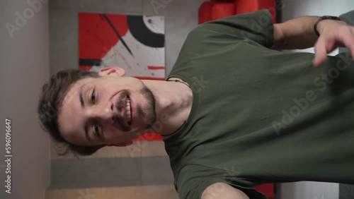 One man young adult caucasian male standing at home with brown hair mustaches and beard looking to the camera happy smile confident talk real people green t shirt UGC selfie user generated content