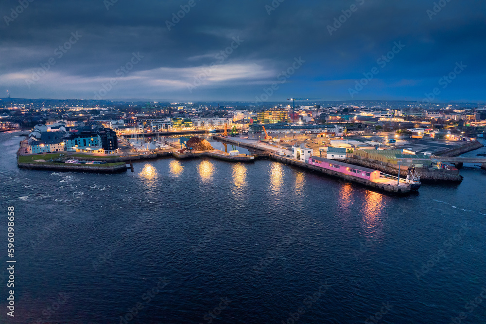 Panorama image of Galway port at night. Aerial view. Popular educational center and tourist hub with vivid night life. Dark sky and light reflection in water.